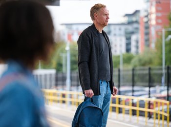 A man standing on a train station platform staring into the distance on a bright day