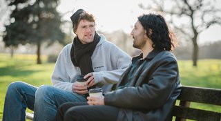 Two men sitting on a bench outside talking (Walk-4888_AR)
